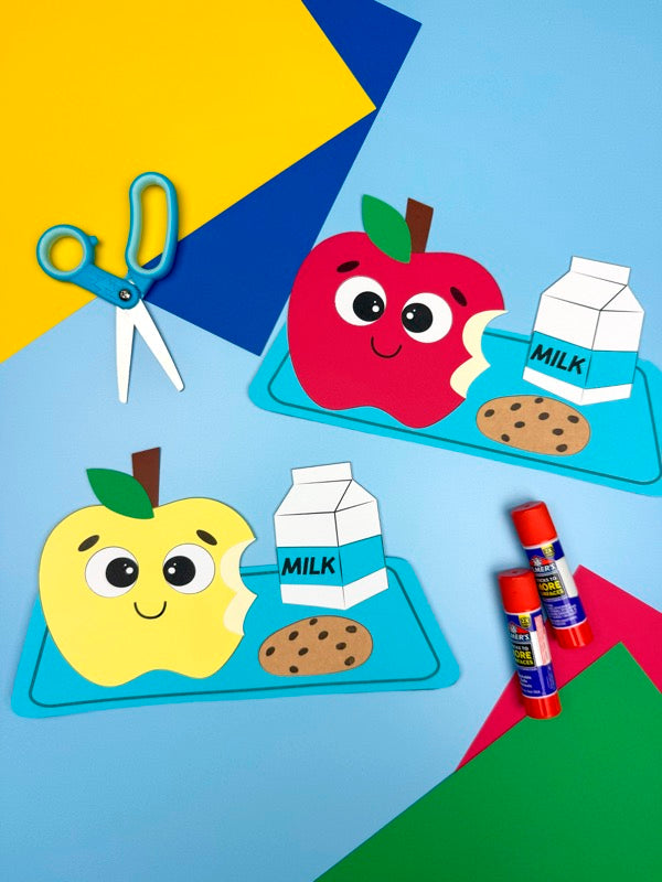 Children's craft project with paper apples, milk cartons, cookies, and scissors on a colorful background.