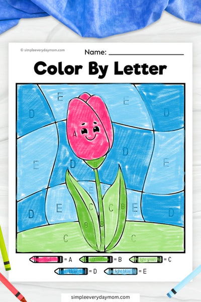 A "Color by Letter" worksheet of a smiling pink tulip with a green stem and leaves, set against a blue sky, with colors filled in according to letter-coded sections.