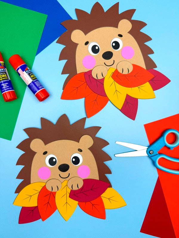 Children's craft project with hedgehog cutouts and fall leaves on a blue background.
