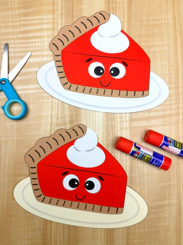 Two paper pie cutouts with faces on a wooden surface with scissors and markers.