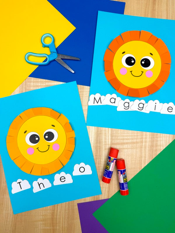Children's craft project with sun and letter cloud cutouts, scissors, and glue sticks on a wooden surface.
