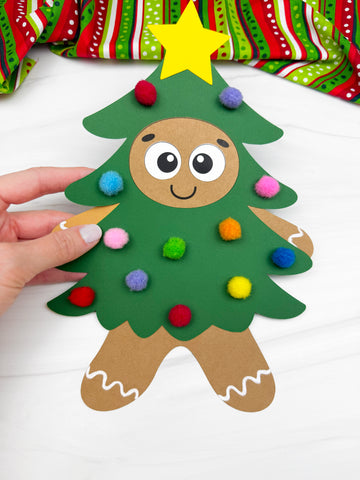 hand holding gingerbread man disguised as a Christmas tree. White background with red and green fabric on top. 