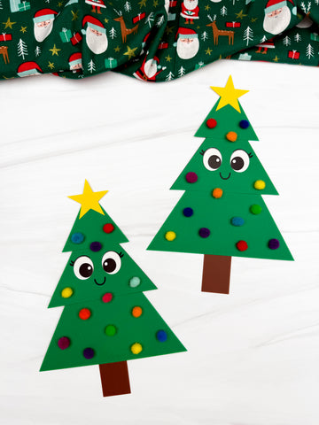 Two paper Christmas trees with googly eyes and a star on a white background, with a festive fabric roll in the background.