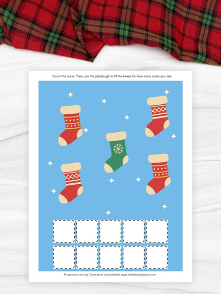 Educational play dough counting worksheet with Christmas stockings on a blue background, placed on a red plaid fabric.