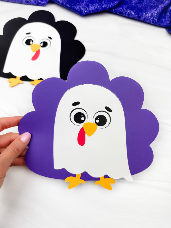 Hand holding a paper craft of a turkey disguised as a ghost on a white background