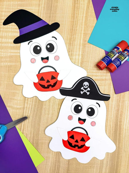 Two trick or treating ghosts on wood background with paper, scissors and glue in the background