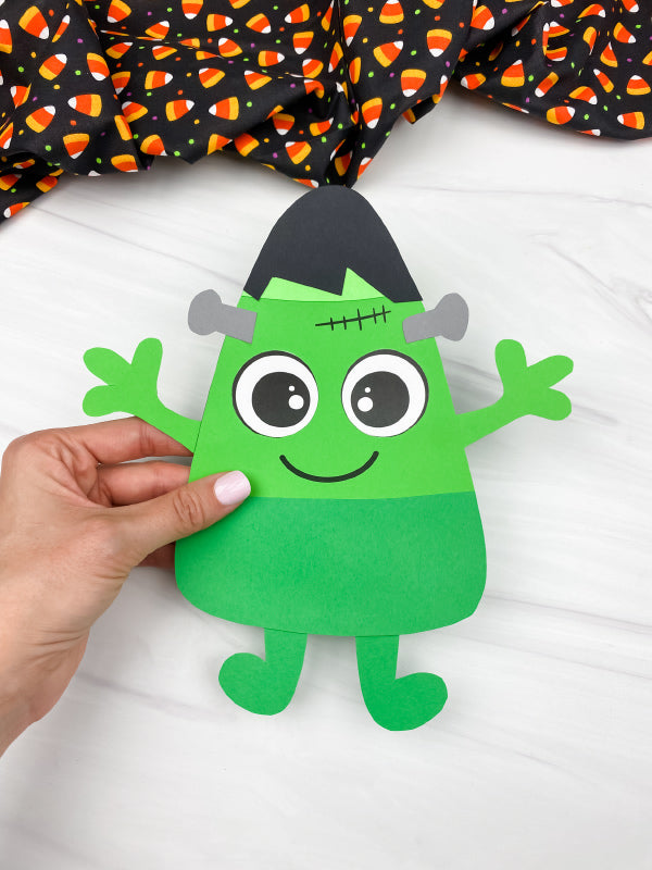 hand holding Frankenstein candy corn craft with white background and Halloween fabric on top.