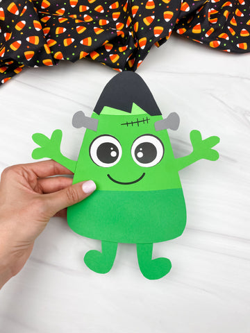 hand holding Frankenstein candy corn craft with white background and Halloween fabric on top.