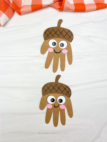 Handprint acorns craft on a white background with an orange and white checkered cloth.