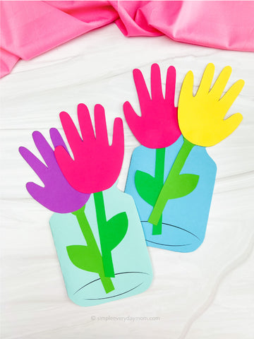 2 handprint flower card crafts on white background with pink fabric on top