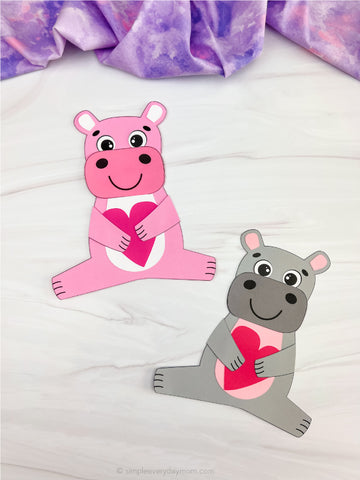 Two hippo Valentine paper crafts on white background with purple fabric