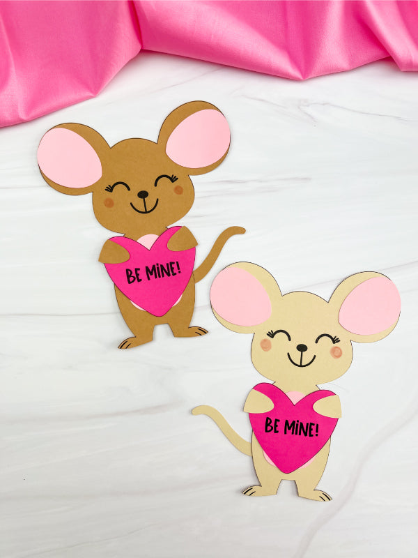 Two paper mouse cutouts with pink hearts and 'Be Mine!' text on a white background.