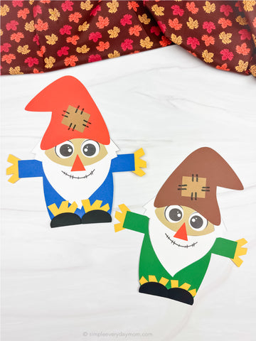 Two colorful paper cutout gnomes on a white background with a patterned fabric border.