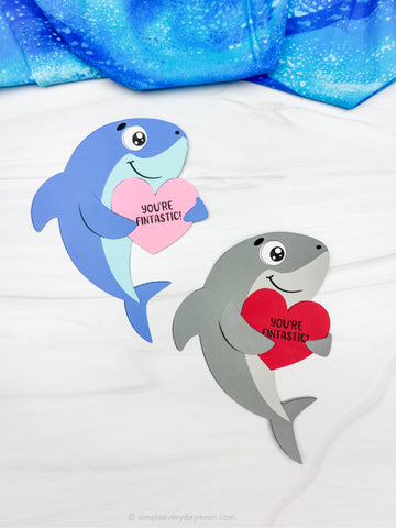 Two shark Valentine crafts on a white background with blue fabric