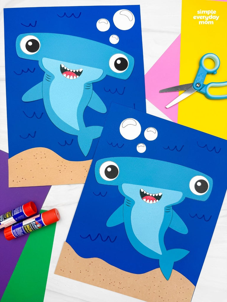 Two hammerhead shark crafts with glue and scissors on a colorful background.