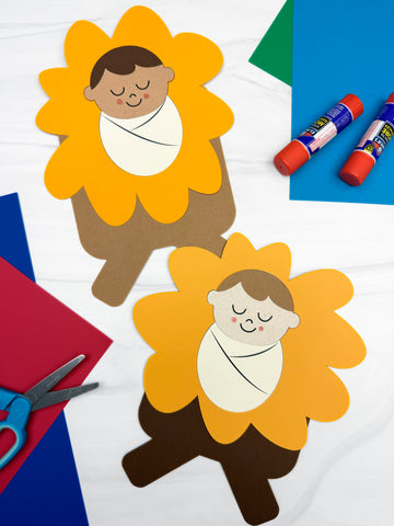 Children's baby Jesus in a manger craft, glue sticks, and scissors on a colorful background.
