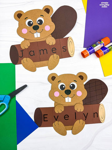 Two beaver name crafts on marble background with colored paper, glue sticks, and scissors 