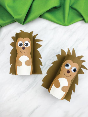 Two tp roll hedgehog crafts on a white surface with green fabric in the background