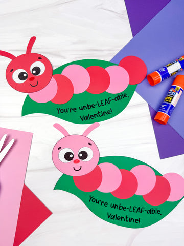 Two colorful caterpillar-shaped Valentine's Day craft on a white background with colored paper, scissors, and glue sticks. 