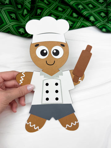 hand holding a gingerbread man disguised as a baker craft, on white background with green fabric. 