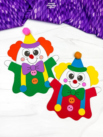 Two colorful clown ghost disguise crafts displayed on a white fabric background with a purple patterned fabric at the top. One clown has red hair, a purple bow tie, green outfit, and blue hat; the other has yellow hair, a green bow tie, red outfit, and blue hat.