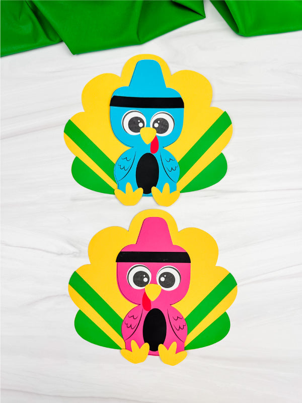 Two turkeys disguised as crayon crafts on white background with green fabric on top. 