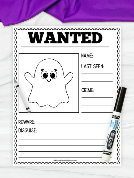 A printable Halloween-themed 'WANTED' poster with a cartoon ghost outline, shown on a white surface with a purple fabric corner at the top and two markers placed around it.
