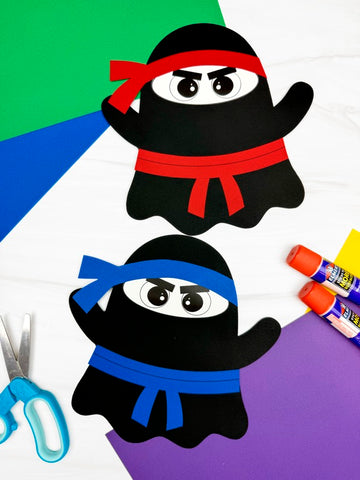 Two paper cutout ghost ninjas with colored belts on a colorful background with scissors and glue sticks.