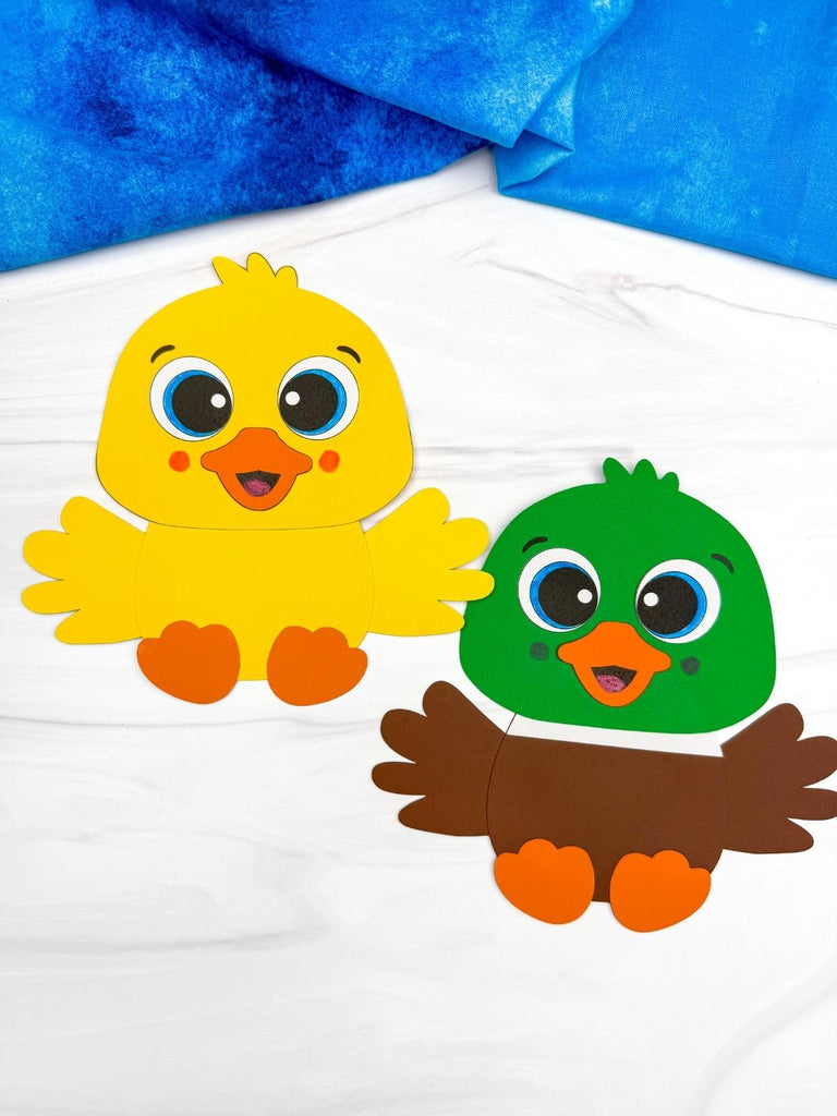 Two duckling paper crafts on white background with blue fabric on top