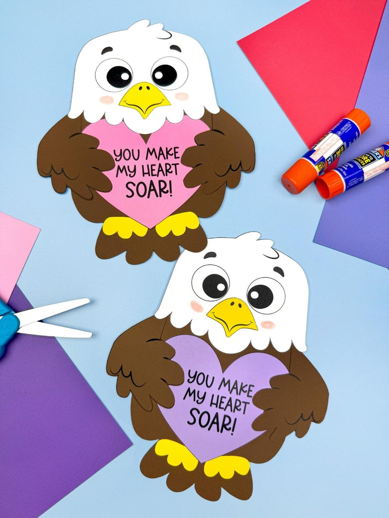 Two paper cutouts of eagles holding hearts with 'You Make My Heart Soar!' text, surrounded by craft supplies on a colorful background.