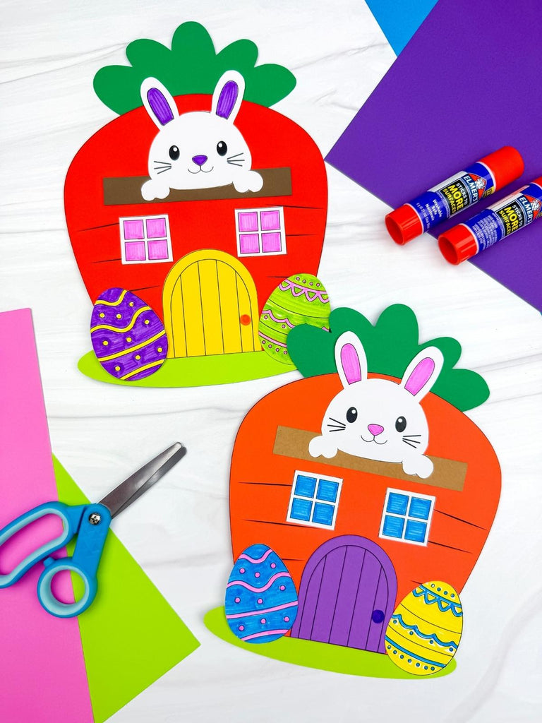 Colorful paper craft of a rabbit in a carrot house with glue sticks and scissors on a white background