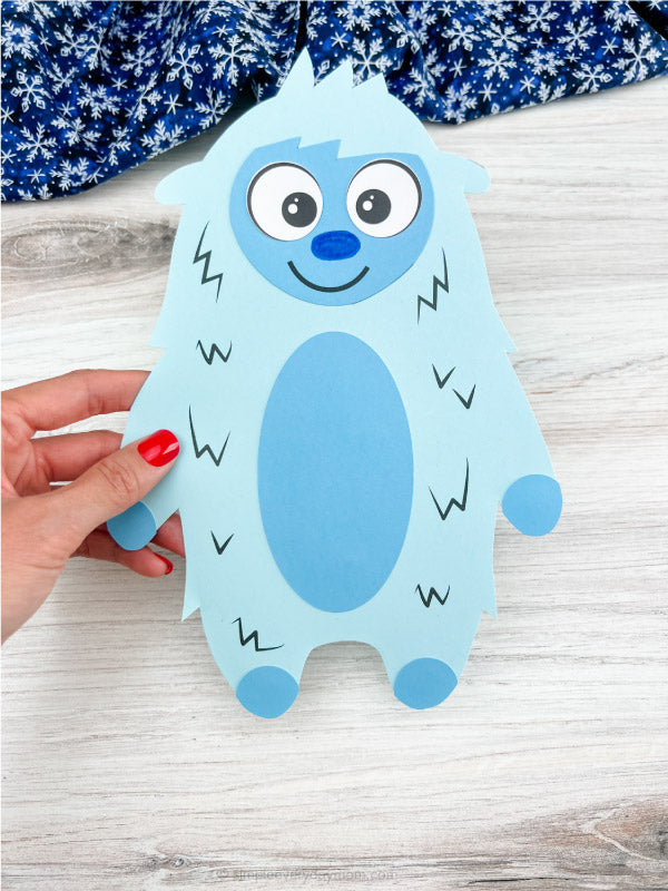 Blue Yeti paper craft held by a hand on a wooden surface with a blue and white patterned fabric in the background.