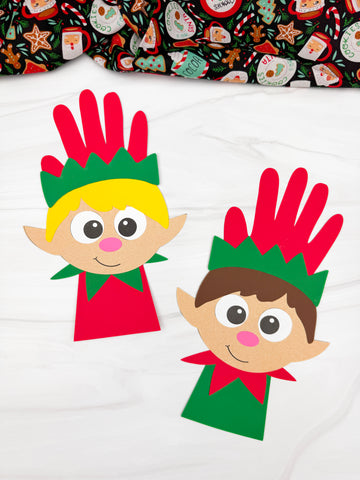 two boy handprint elf crafts on marble background with fabric on top
