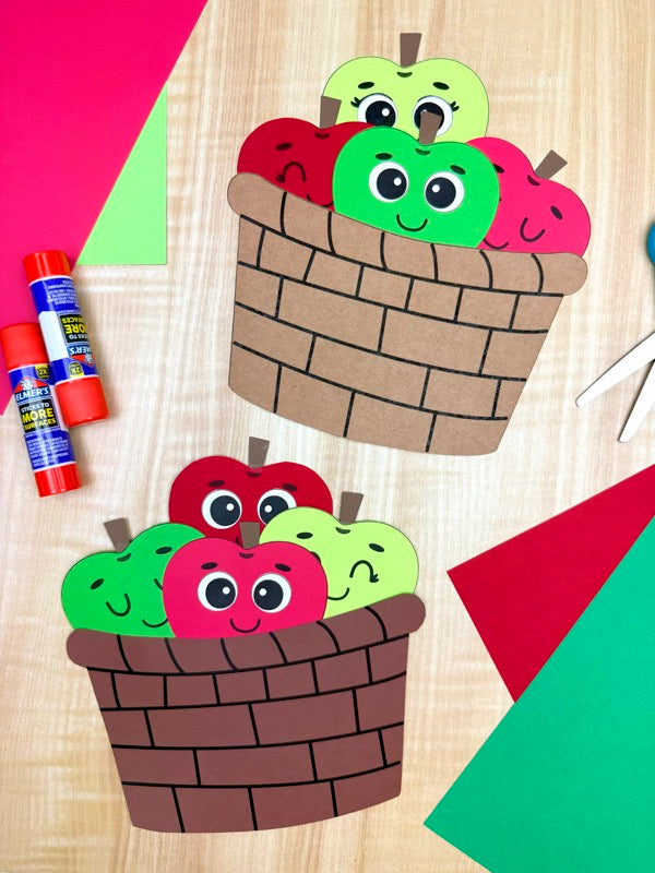 Colorful paper apples and baskets on a wooden surface with craft supplies.