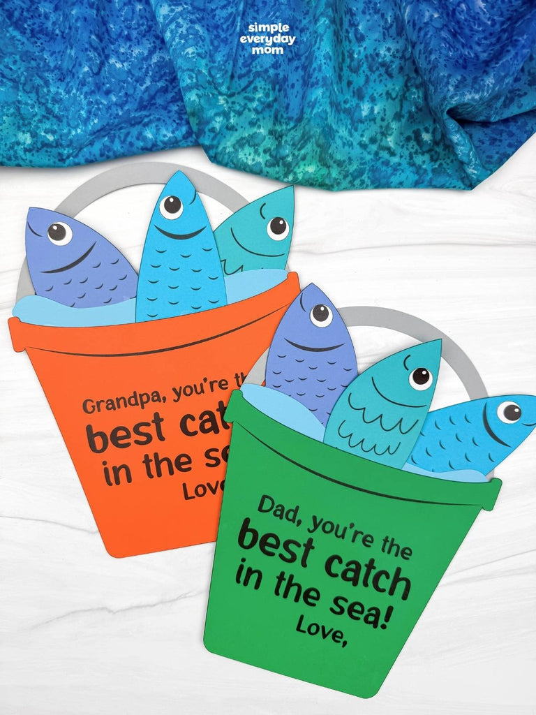 Two Father's Day fishing bucket crafts on white background with blue fabric on top