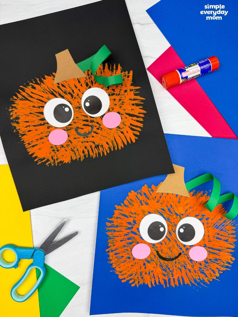 Two fork painted pumpkin crafts on colorful background with scissors and glue
