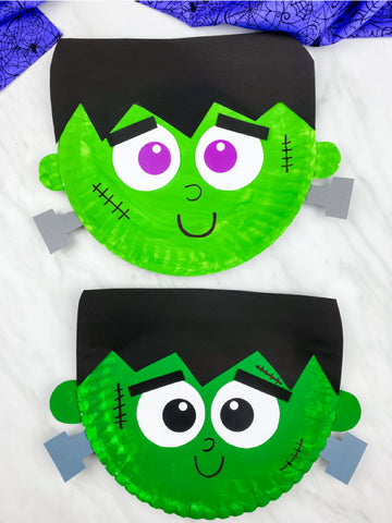 Two green paper plate Frankenstein faces on a white background with purple fabric on top