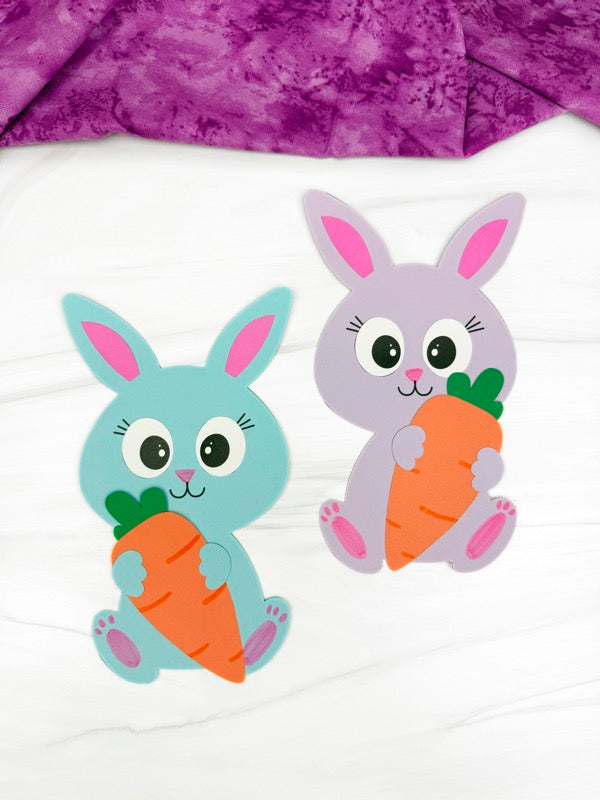 Two colorful paper bunny crafts holding carrots on a white background