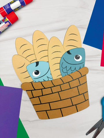 Paper fish and bread in a basket craft on a colorful background with glue and scissors.