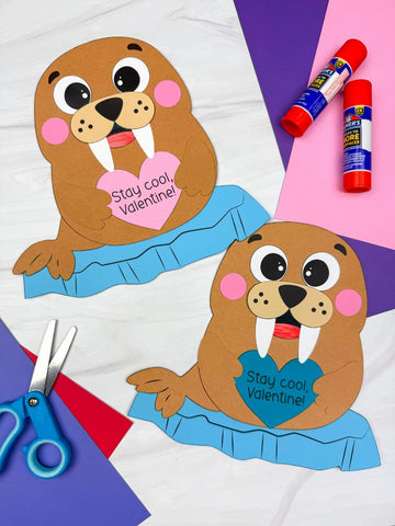 Two paper walrus crafts with heart-shaped messages on a colorful background with glue sticks and scissors.