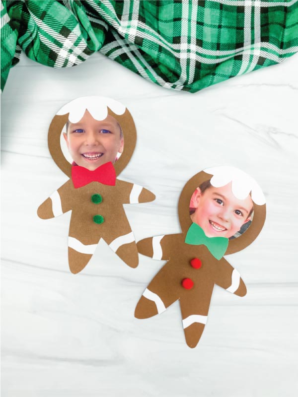 Two gingerbread man photo crafts with photos of children inside, on a white surface with a green plaid fabric in the background.