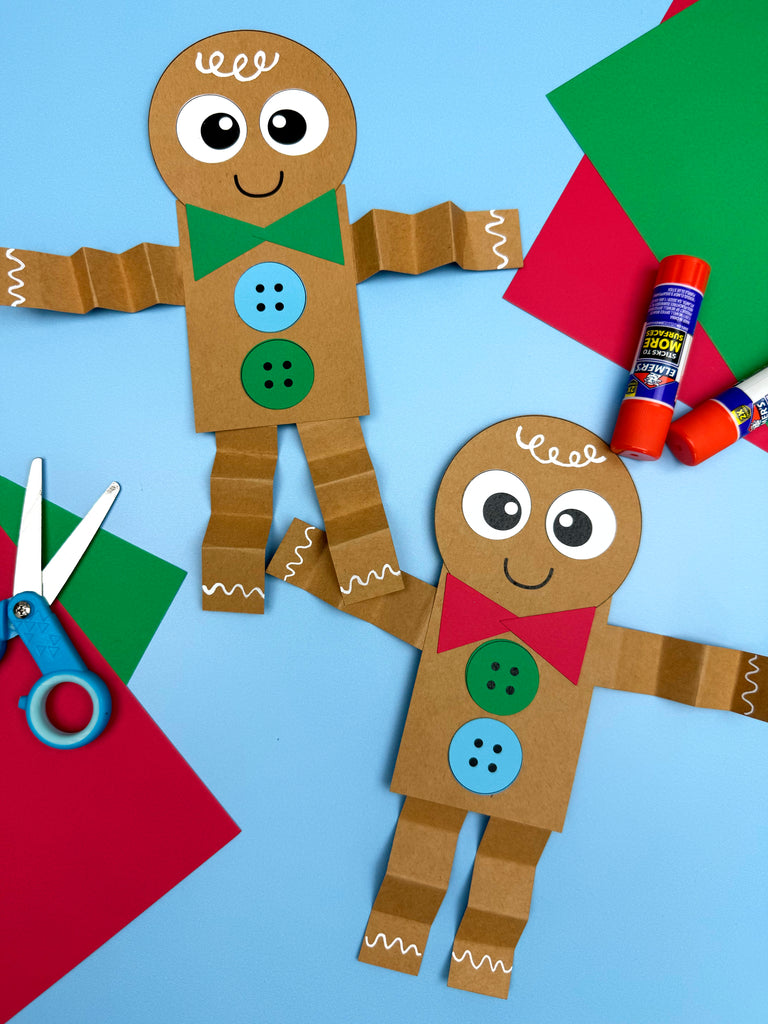 two gingerbread man shape crafts on blue background with scissors, glue and paper. 