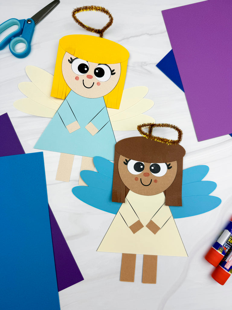 Two paper angel crafts on a white background with scissors and glue sticks.