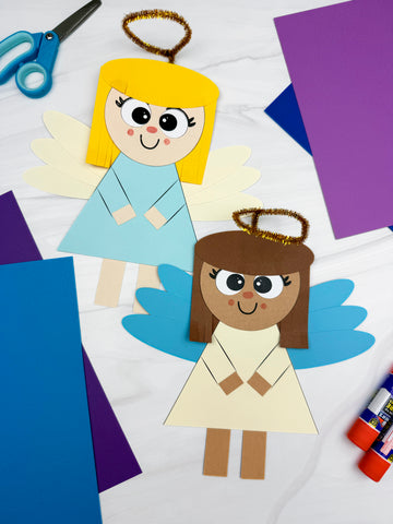 Two paper angel crafts on a white background with scissors and glue sticks.