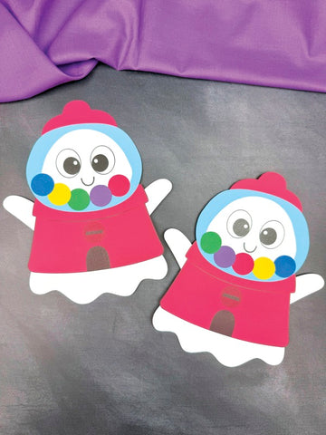 Two colorful paper cutouts of ghosts disguised as a gumball machine on a purple background