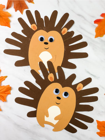 2 handprint hedgehog crafts on marble background with leaves