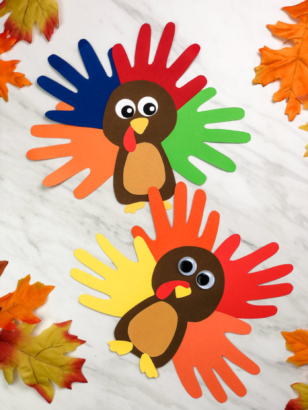 Handmade turkey decorations made from colored paper on a white background with fall leaves.