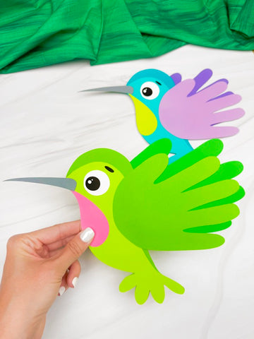 hand holding green hummingbird handprint craft with 2nd one in the background