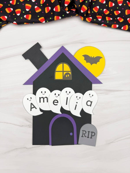 Halloween-themed haunted house with ghosts spelling "Amelia" on a white background
