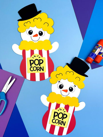 Two popcorn snowman disguise crafts on blue background with colored paper, scissors, & glue. 